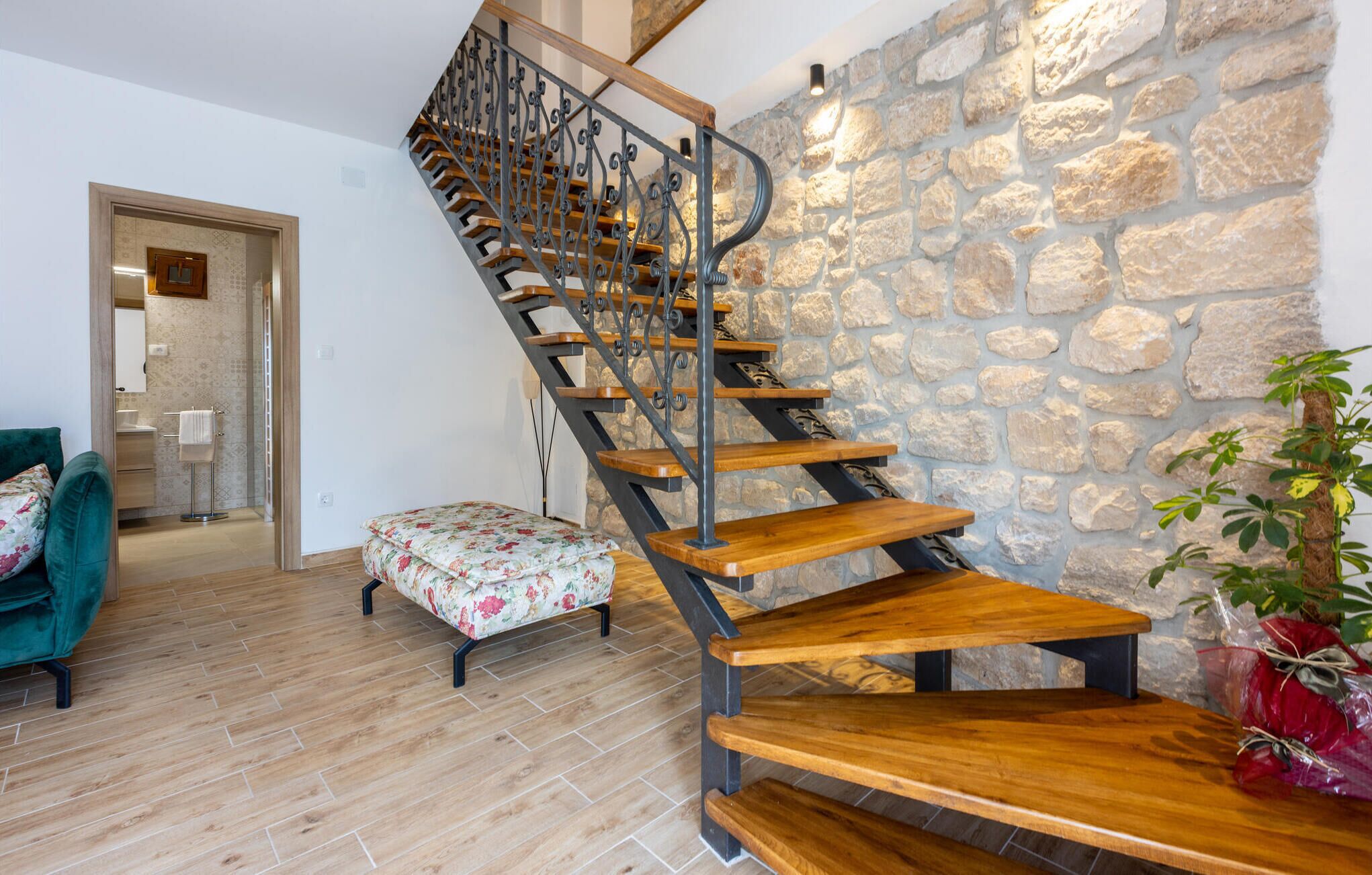 A staircase with wooden steps and metal railings, leading to a room with a stone wall and a wooden floor.