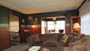 Una sala de estar acogedora con un sofá marrón, una mesa de centro de madera y una zona de comedor con mantel a cuadros.