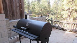 Una parrilla RiverGrille al aire libre con termómetro digital, frente a un seto de madera y árboles.