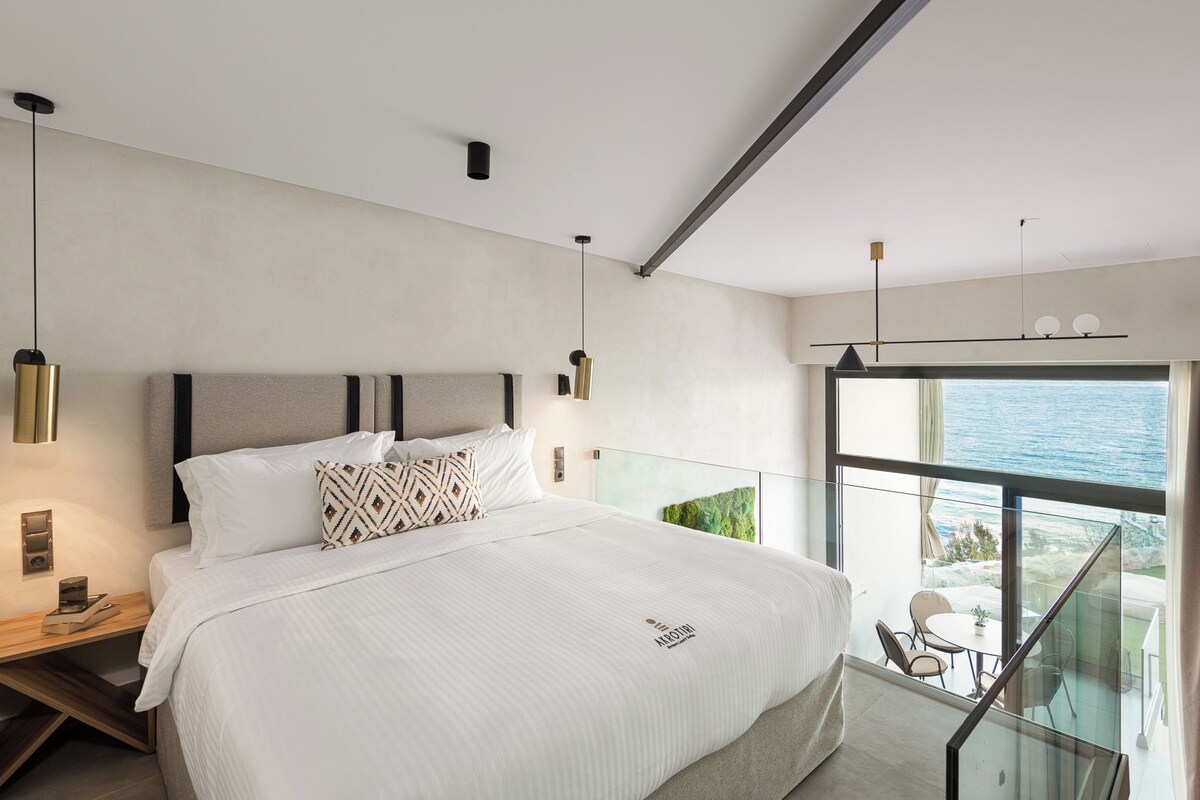 A modern bedroom with a large bed, bedside tables, and a balcony with a view of the sea.