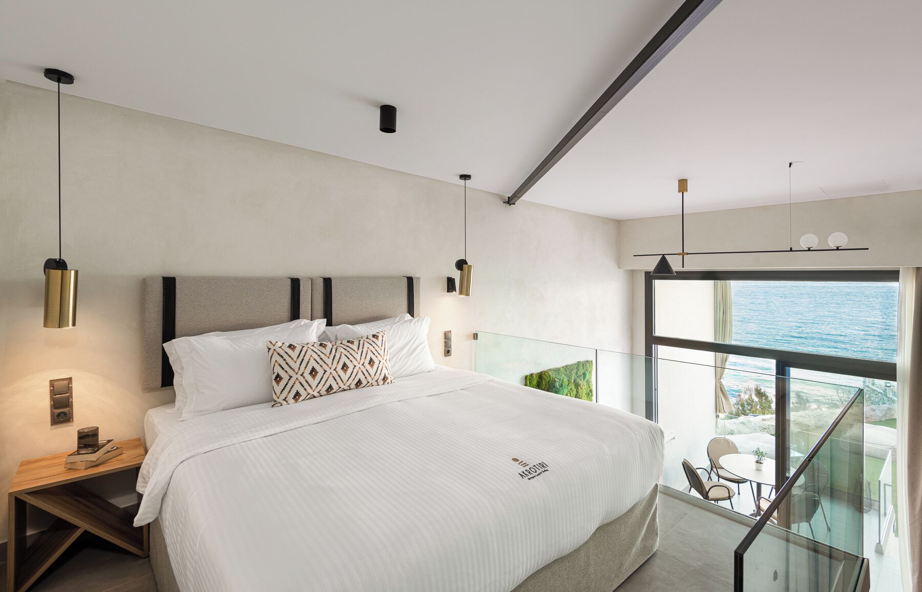 Un dormitorio moderno con una cama grande, mesitas de noche y un balcón con vista al mar.