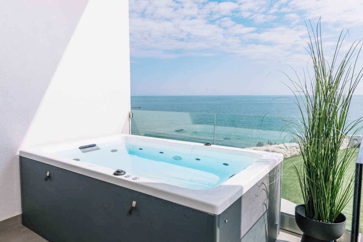 A spa tub with a view of the ocean, a potted plant, and a balcony with a railing.