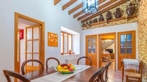 A dining area with a wooden table, chairs, a fruit bowl, and a view of a kitchen and staircase. - SON SEGUÍ - Villa with private pool in Alaró with free WiFi (Alaro)