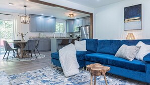 A modern living room with a blue sofa, a wooden coffee table, and a dining area with a table and chairs. - Modern 3BR Family Home, Fenced Yard, Pets Friendly + 15 min to Stone Mountain (Snellville)