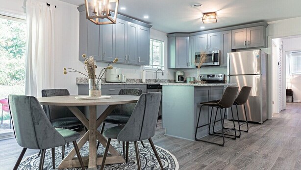 A modern kitchen with grey cabinets, stainless steel appliances, and a round dining table with chairs. - Modern 3BR Family Home, Fenced Yard, Pets Friendly + 15 min to Stone Mountain (Snellville)