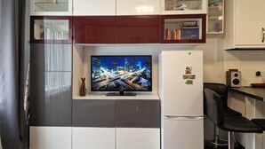 Una cocina moderna con televisión integrada, un refrigerador y una zona de comedor con dos taburetes de bar.