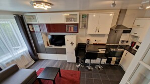 Un espacio habitable pequeño con sofá, una mesita, kitchenette y televisor.