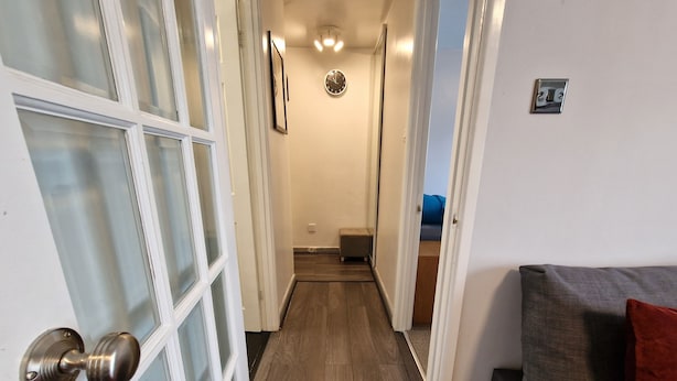 Un pasillo con suelo de madera, una puerta con paneles de vidrio esmerilado y una pequeña zona de estar con un cojín y una almohada.