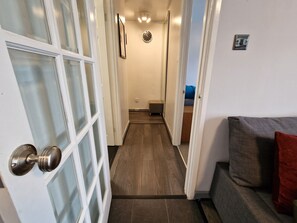 A hallway with a wooden floor, a door with frosted glass panels, and a small seating area with a cushion and a pillow.