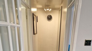 Un pasillo con piso de madera, un reloj en la pared y una puerta con paneles de vidrio esmerilado.