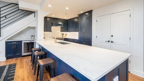 Een moderne keuken met donkerblauwe kastjes, een wit marmer eiland en een roestvrijstalen afzuigkap.