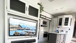 A modern kitchen with built-in appliances, a flat-screen TV mounted on the wall, and a view of a bridge and harbor through the window. - Johnny Love, Modern and Bright Paradise RV (San Diego)