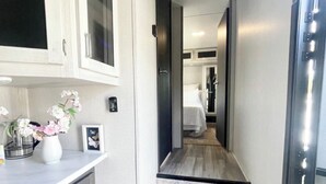 A narrow hallway with a staircase leading to a bedroom. There are cabinets on the left, a small table with flowers, and a framed picture. - Johnny Love, Modern and Bright Paradise RV (San Diego)
