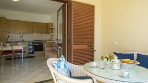 Un coin repas avec des chaises en osier et une table en verre, une cuisine avec des meubles en bois et une porte coulissante en bois.
