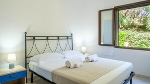 Un lit bien fait, avec du linge de lit blanc et deux serviettes enroulées, une table de chevet avec une lampe et une fenêtre donnant sur un paysage verdoyant.