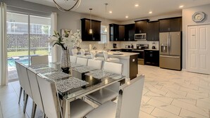 A modern kitchen with dark cabinets, stainless steel appliances, and a dining area with a glass table and white chairs.