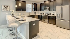 A modern kitchen with dark cabinets, stainless steel appliances, a marble countertop, and pendant lighting.