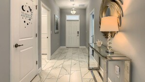 A hallway with a marble floor, a white door with a moon and stars decal, a framed picture on the wall, and a console table with a lamp and decorative items.