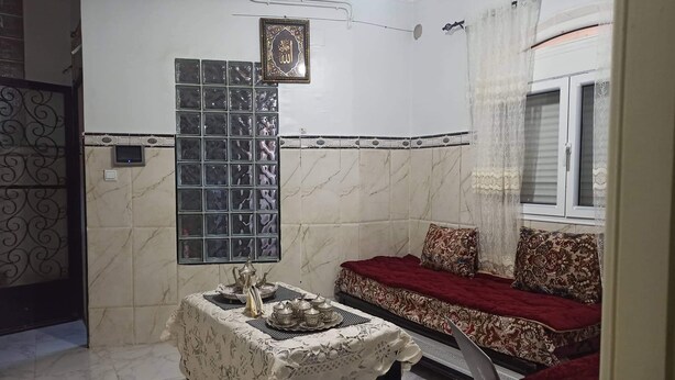 A room with a sofa, a table with a laptop, a decorative wall, and a window with curtains. - Joli F1 Convivial,propre Neuf , Indépendant, Équipée, Stratégique de (Tlemcen)