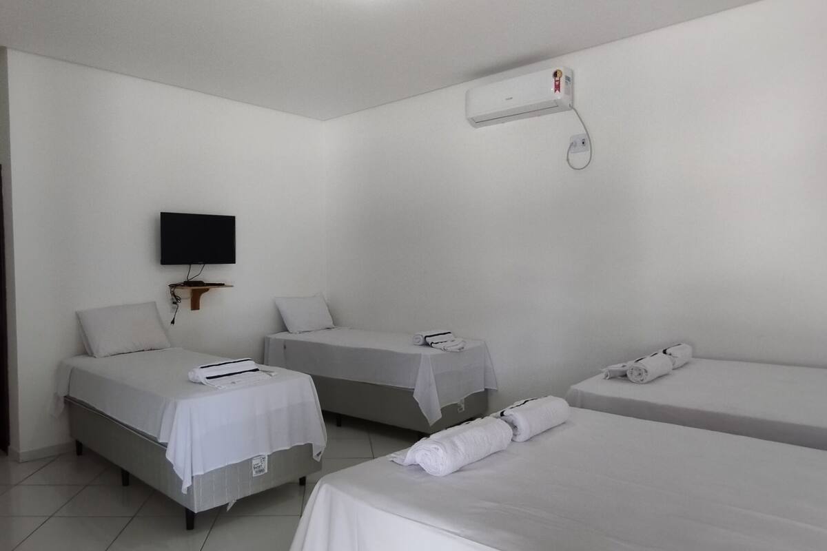 A hotel room with two single beds, a bench, a flat-screen TV, and a wall-mounted air conditioner.