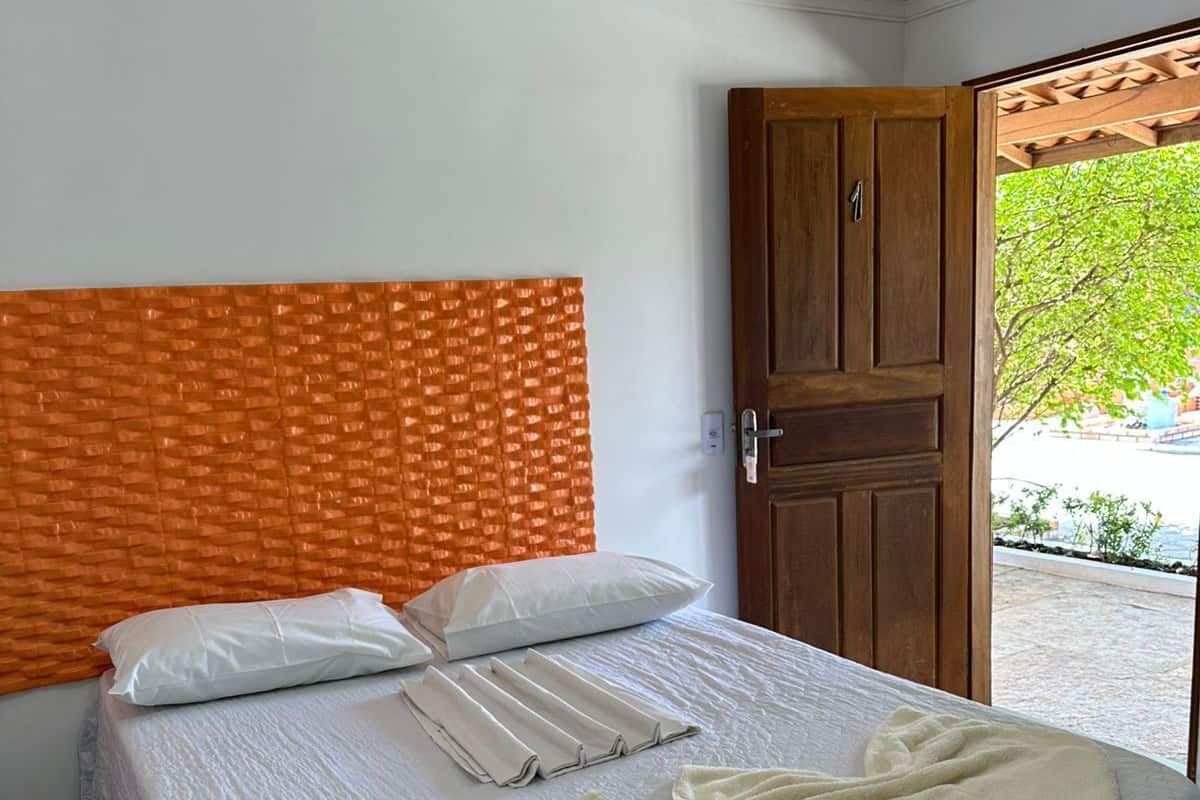 A neatly made bed with white linens, a beige throw blanket, and a towel folded on the bed.