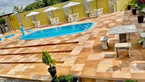 Un'area piscina con solarium piastrellato, arredi da esterno e piante in vaso.