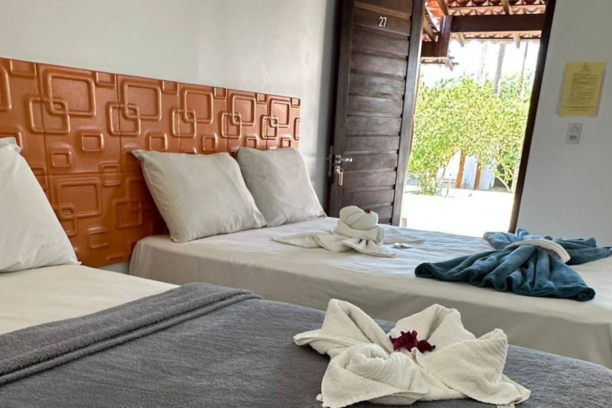 A hotel room with two beds, a patterned headboard, and a view of greenery outside.