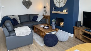 A modern living room with a grey sofa, wooden coffee table, and a TV on a wooden stand. - Worthing Beach 180 - 2 bed Seafront With Parking (Worthing)