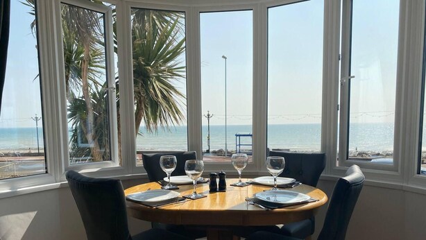A dining area with a table set for four, overlooking a beach. - Worthing Beach 180 - 2 bed Seafront With Parking (Worthing)