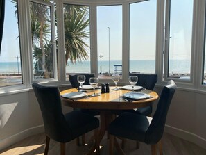 A dining area with a table set for four, overlooking a beach. - Worthing Beach 180 - 2 bed Seafront With Parking (Worthing)