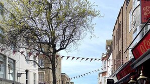 A bustling street with outdoor seating at various cafes, lined with brick buildings and a tree in the center. - Worthing Beach 180 - 2 bed Seafront With Parking (Worthing)