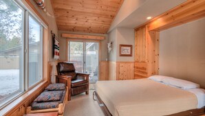 A bedroom with a large bed, a wooden ceiling, a window with a view of the outside, and a chair with cushions. - Single Level Sunriver Retreat , A/C, Hot Tub, SHARC, and Bikes (Sunriver)