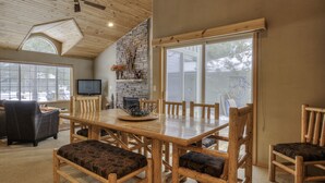 A dining area with a wooden table and chairs, a fireplace, and large windows. - Single Level Sunriver Retreat , A/C, Hot Tub, SHARC, and Bikes (Sunriver)