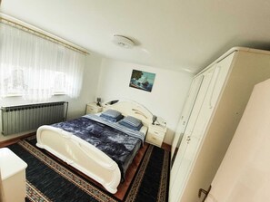A bedroom with a bed, bedside tables, a radiator, a wardrobe, and a window with curtains. - Beautiful 1-bed Apartment in Sveta Nedelja (Sveta Nedelja)