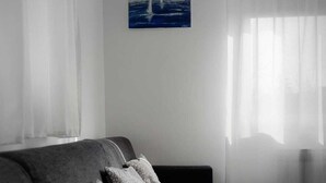 A minimalist living room with a grey sofa, a small white table, and a painting of a sailboat on the wall. - Beautiful 1-bed Apartment in Sveta Nedelja (Sveta Nedelja)