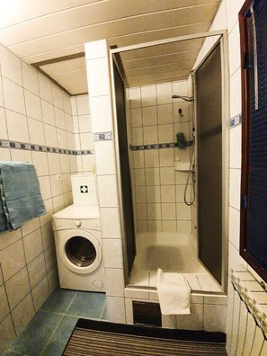 Un baño pequeño con lavadora, cabina de ducha y perchero.
