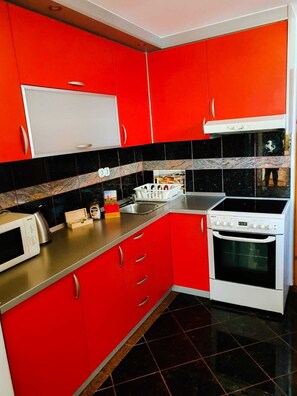 A kitchen with red cabinets, a white microwave, a stove, and black and white tiles. - Beautiful 1-bed Apartment in Sveta Nedelja (Sveta Nedelja)