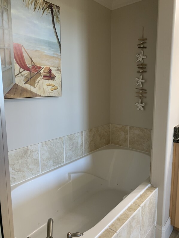 Une salle de bain avec une baignoire, un tableau représentant une scène de plage et une étoile de mer décorative fixée au mur.
