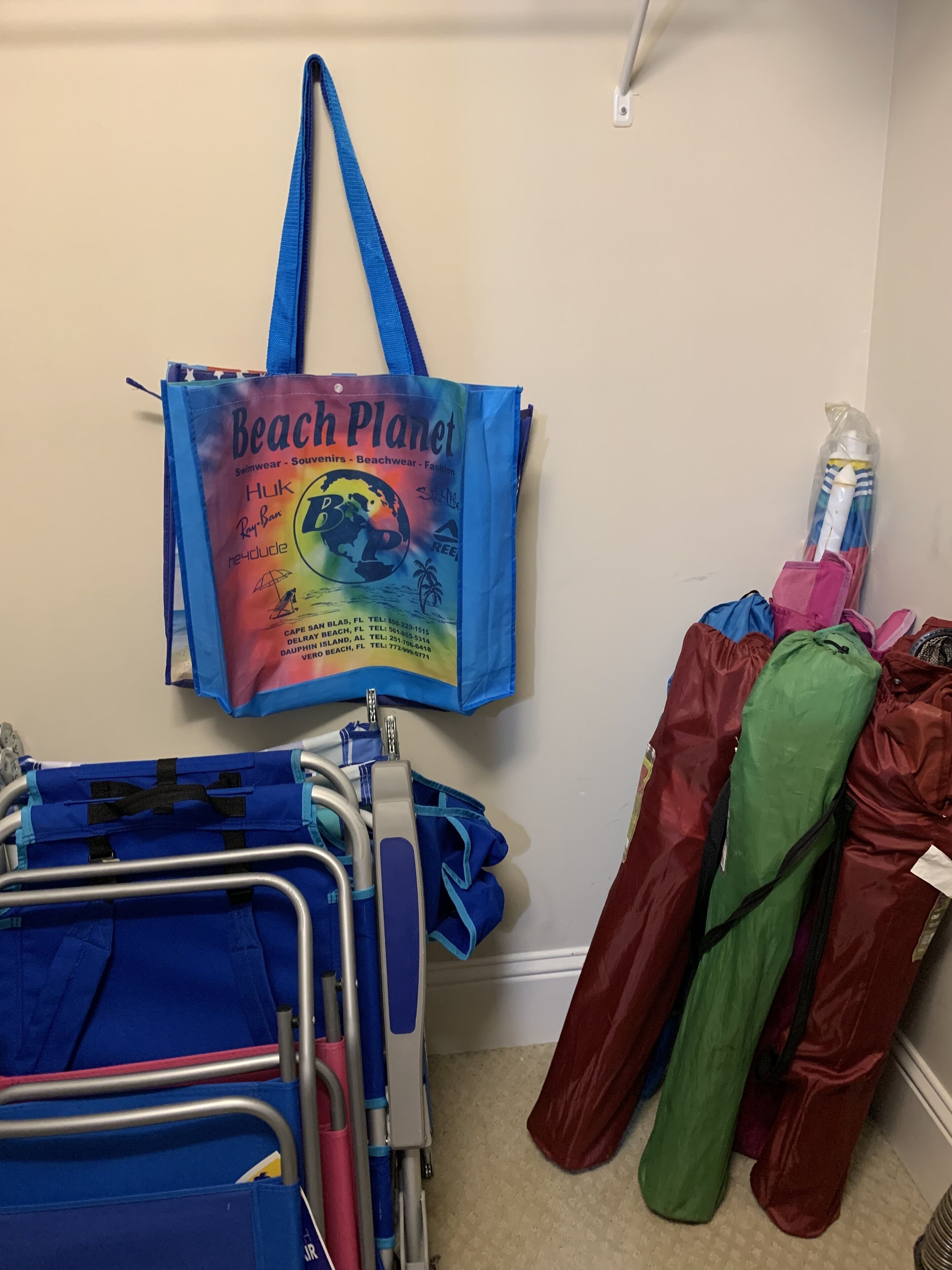 Ett rum med en blå tygkasse med strandmotiv som hänger på väggen, en metallvagn med blå och röda föremål och en grön och röd väska som står lutad mot väggen.