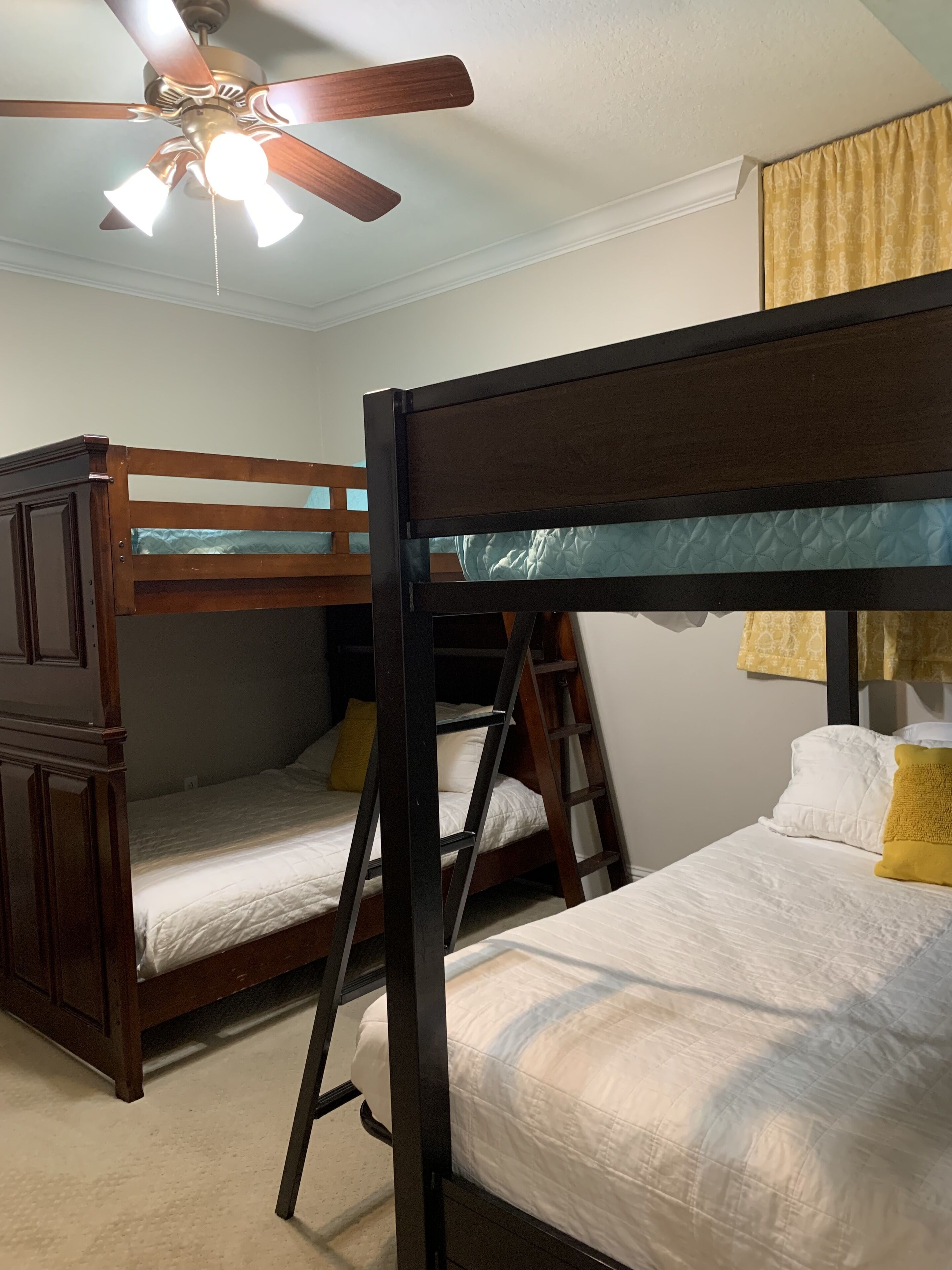 Een slaapkamer met stapelbed, een plafondventilator, houten meubels en een raam met gordijnen.