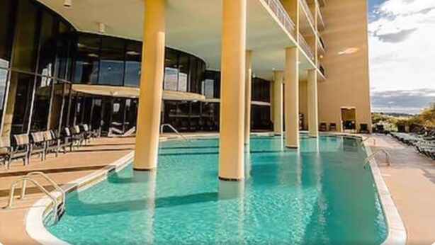 Une piscine à l’eau d’un bleu cristallin, entourée de piliers de couleur beige et de chaises longues.