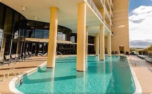 Une piscine à l’eau d’un bleu cristallin, entourée de piliers de couleur beige et de chaises longues.