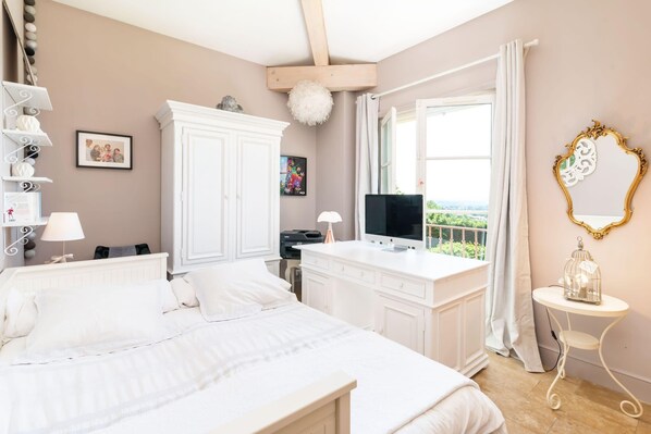 A bedroom with a large bed, a desk with a computer, a TV, and a window with a view.