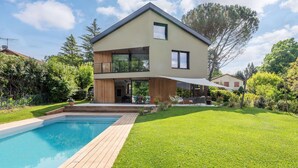Et moderne hus med to etager, swimmingpool, træterrasse og en velplejet græsplæne.