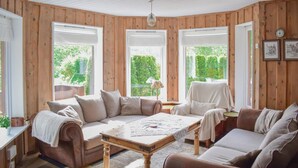 Ein gemütliches Zimmer mit Holzwänden, einem braunen Sofa, einem Holztisch und Blick ins Grüne.