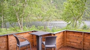 Eine Holzterrasse mit zwei Korbstühlen und einem Tisch, mit Blick auf einen See, in der Ferne ein Boot.
