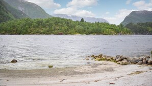 Eine Küstenlandschaft mit felsiger Küste, einem kleinen Gebäude und einem bewaldeten Hügel im Hintergrund.