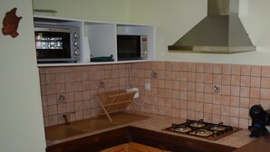 A kitchen with a gas stove, a microwave, and a built-in oven. There is a wooden cabinet with red handles and a brick backsplash.