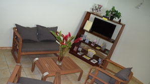 A living room with a sofa, two armchairs, a coffee table, and a TV stand with books and decorative items.