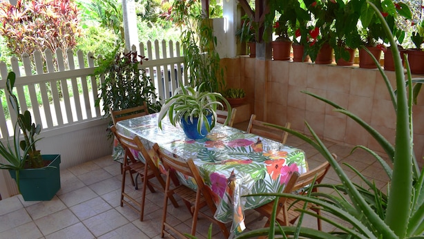 A patio with a table covered in a floral tablecloth, surrounded by wooden chairs.